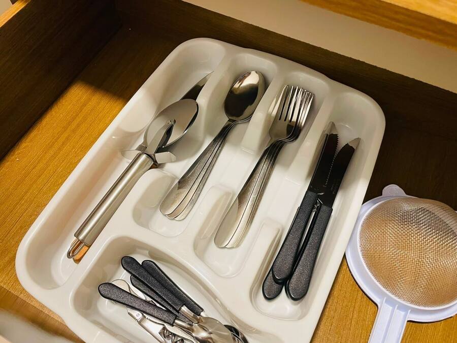 A drawer containing a set of silverware including a spoon, fork, knife, and chopsticks, along with a strainer.