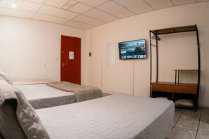 Habitación de hotel con dos camas, un televisor montado en la pared, un estante de madera y una puerta roja.
