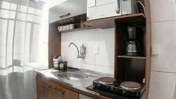 Uma cozinha compacta com pia, cafeteira e micro-ondas.