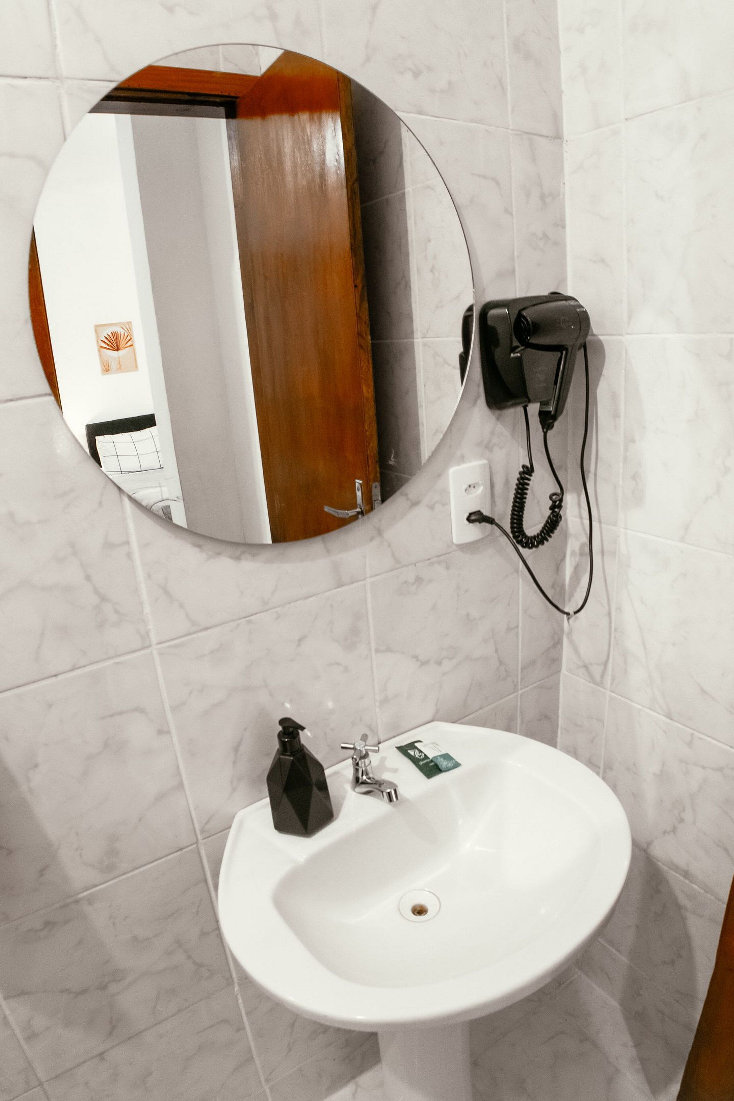 Un baño con un espejo redondo, un lavabo blanco, un teléfono y una pared revestida de mármol.