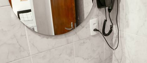 Un baño con un espejo redondo, un lavabo blanco, un teléfono y una pared revestida de mármol.