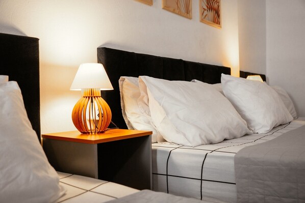 A neatly made bed with white bedding, a wooden bedside table with a lamp, and a black headboard.