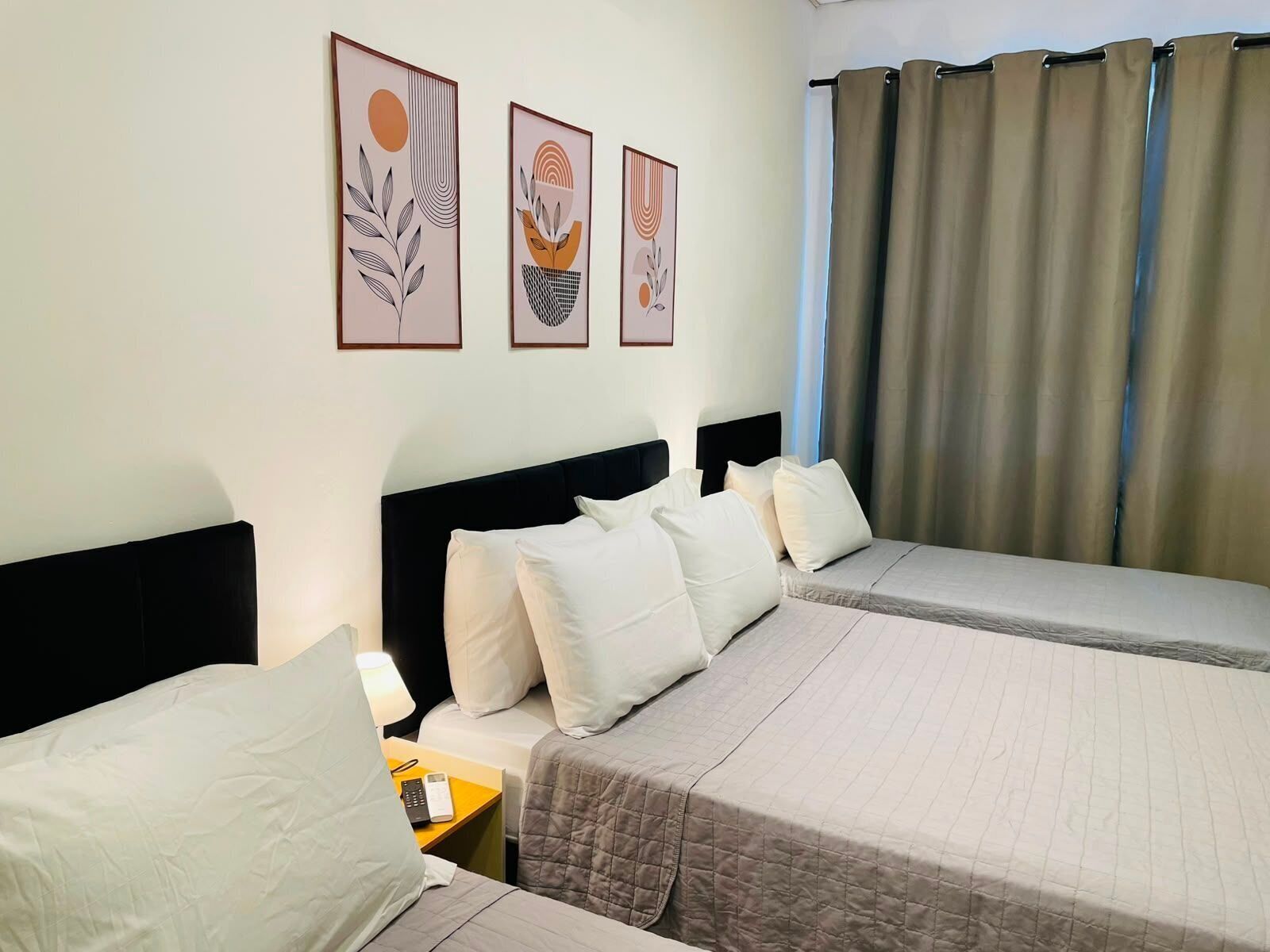 A hotel room with two beds, a nightstand, a telephone, and three framed artworks on the wall.
