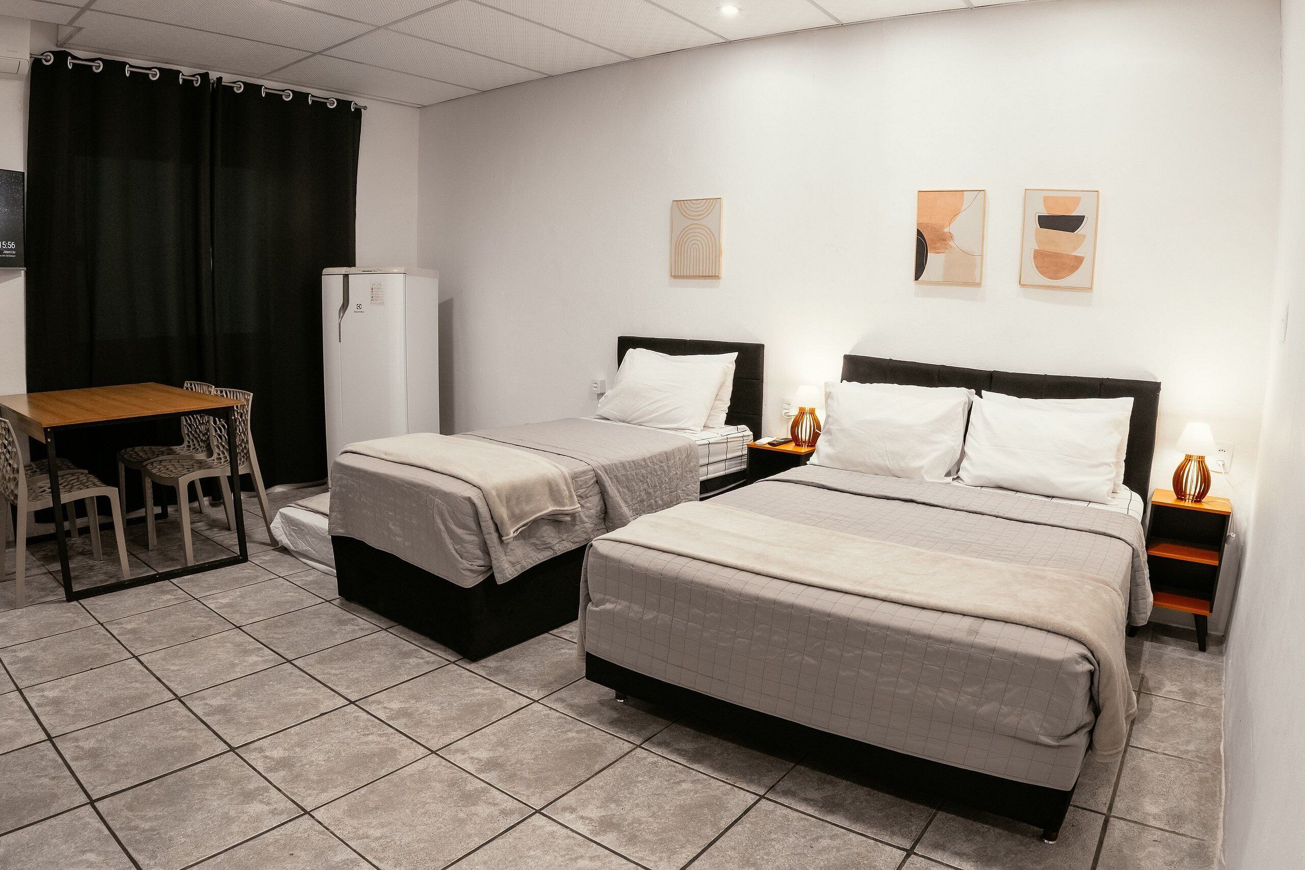 A hotel room with two beds, a desk, chairs, a refrigerator, and artwork on the walls.