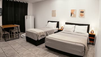 Habitación de hotel con dos camas, un escritorio, sillas, un refrigerador y obras de arte en las paredes.