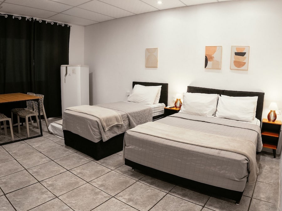 Habitación de hotel con dos camas, un escritorio, sillas, un refrigerador y obras de arte en las paredes.