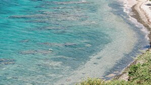 A coastal landscape with clear turquoise waters, a sandy beach, and a rocky outcrop with sparse vegetation.