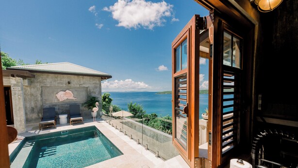 A pool area with a view of the sea, a stone wall, and a wooden door.