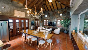 A spacious kitchen with a large wooden table, modern chairs, and a stone wall backdrop.