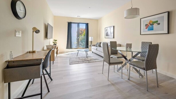 A modern living room with a dining area, a sofa, a coffee table, and a TV mounted on the wall. - Fabulous 2BR ! Free Parking !  30 Min to NYC ! (Newark)