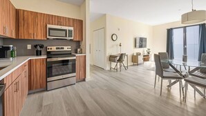 A modern kitchen with wooden cabinets, a microwave, oven, and a dining area with a glass table and chairs. - Fabulous 2BR ! Free Parking !  30 Min to NYC ! (Newark)