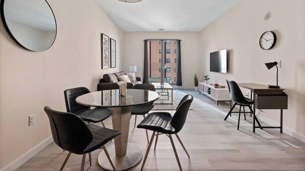 A modern living room with a round glass table, black chairs, a sofa, a TV, and a desk with a lamp. - Marvelous 2BR ! Free Parking !  30 Min to NYC (Newark)