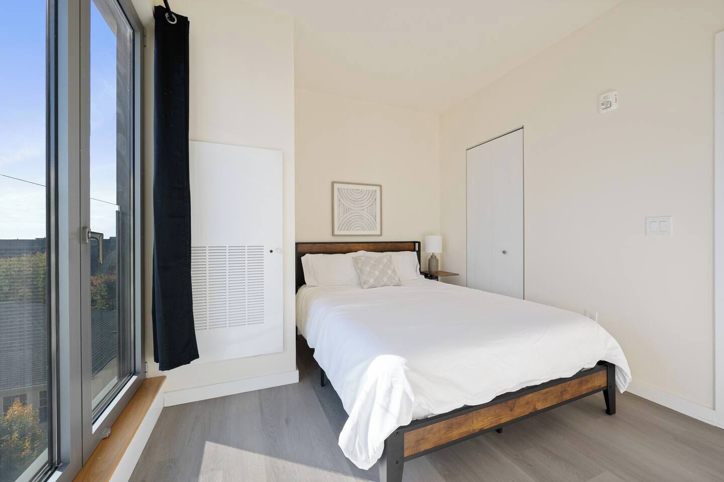 Une chambre à coucher avec un lit, une fenêtre, une porte et une œuvre d’art accrochée au mur.
