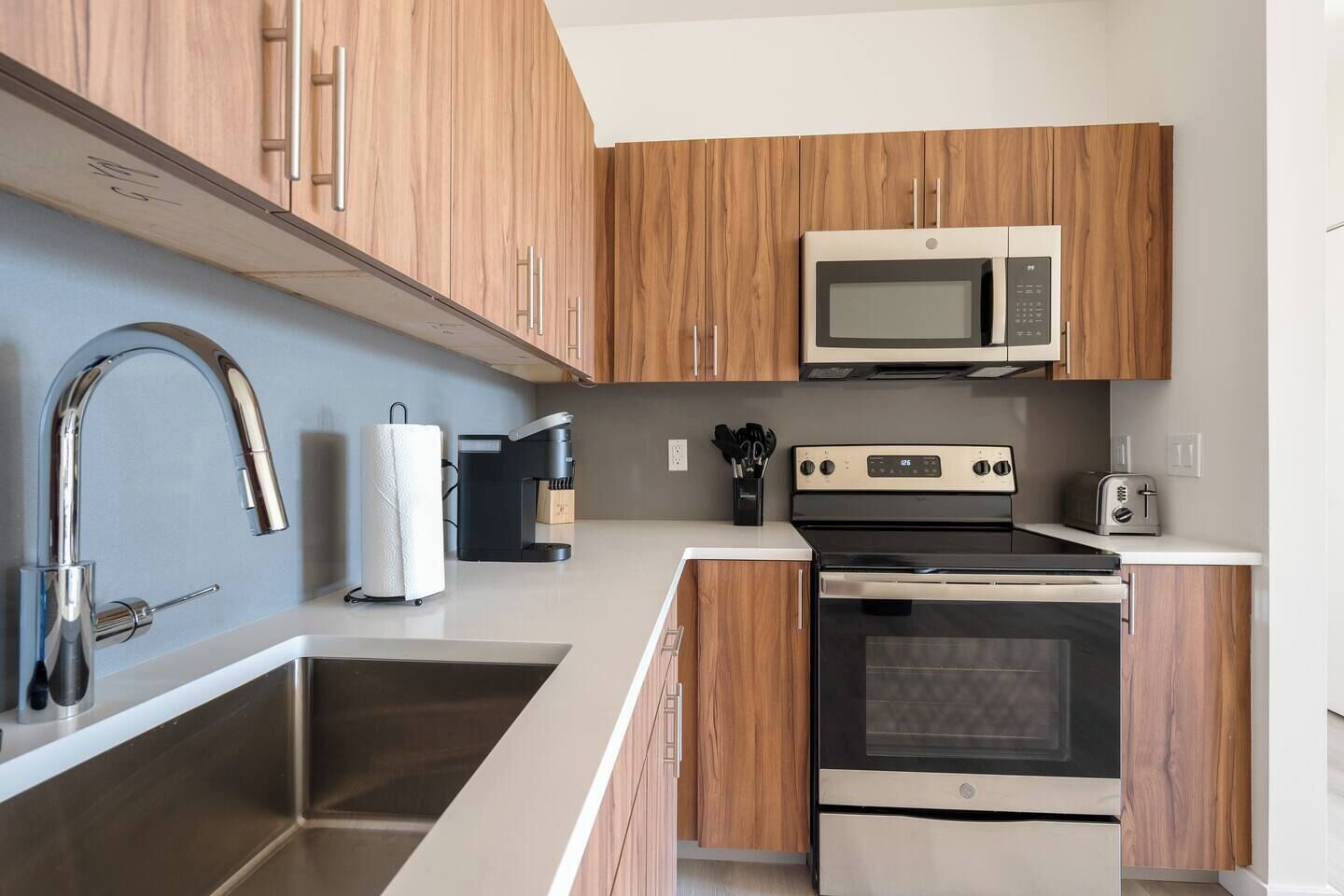 A modern kitchen with wooden cabinets, stainless steel appliances, a microwave, a coffee maker, and a toaster.
