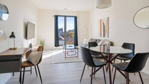 Een moderne woonkamer met een glazen eettafel, zwarte stoelen, een bank en een groot raam met uitzicht op de stad.