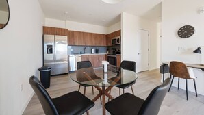 Een moderne keuken met roestvrijstalen apparatuur, een eethoek met een glazen tafel en een klok aan de muur.