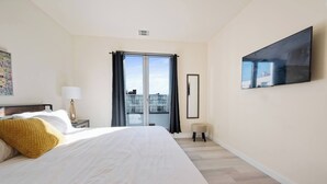 Een hotelkamer met een groot bed, een flatscreen-tv, een balkon met uitzicht en een klein krukje.