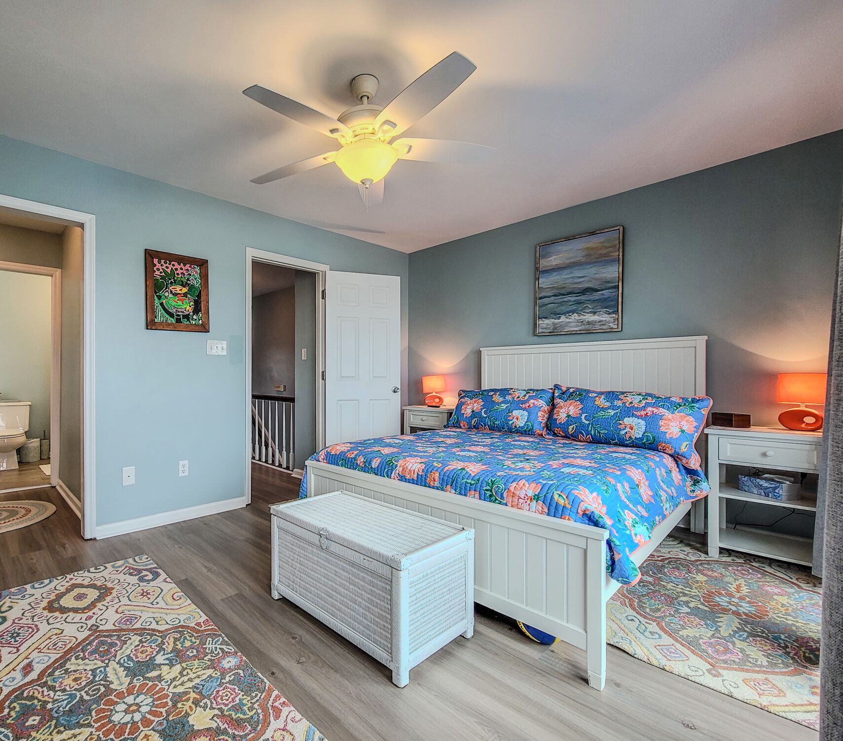 A bedroom with a bed, a ceiling fan, a nightstand, a lamp, a door, and a window.