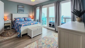 Ein Schlafzimmer mit Bett, Nachttisch, Schminktisch, Kommode, Deckenventilator, Fenster mit Vorhängen und Meerblick.