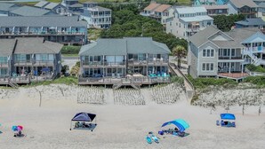 Eine Küstenlandschaft mit Strandhäusern, darunter Häuser mit Balkonen, sowie ein Sandstrand mit Sonnenschirmen und Liegestühlen.