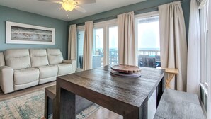 Ein geräumiges Wohnzimmer mit einem großen Holztisch, einem weißen Sofa und einem Deckenventilator.