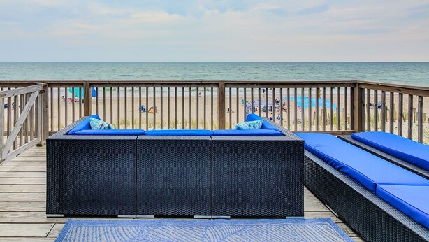 Eine Holzterrasse mit Korbmöbeln und blauen Kissen mit Blick auf einen Strand.