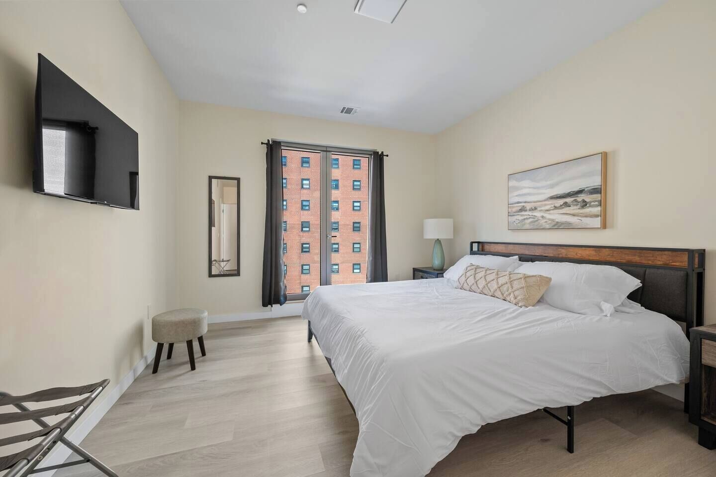 A bedroom with a large bed, a flat-screen TV mounted on the wall, a window with curtains, and a painting on the wall.