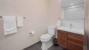 Une salle de bain avec des toilettes, un lavabo et un miroir. Deux serviettes blanches sont suspendues à un porte-serviettes.