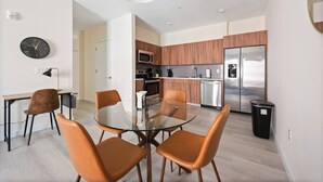 Une cuisine moderne dotée de meubles en bois, d’appareils électroménagers en acier inoxydable et d’une table à manger en verre, accompagnée de quatre chaises.