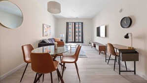 Un salon moderne avec une table ronde en verre, des fauteuils orange, un canapé, un téléviseur et une horloge au mur.