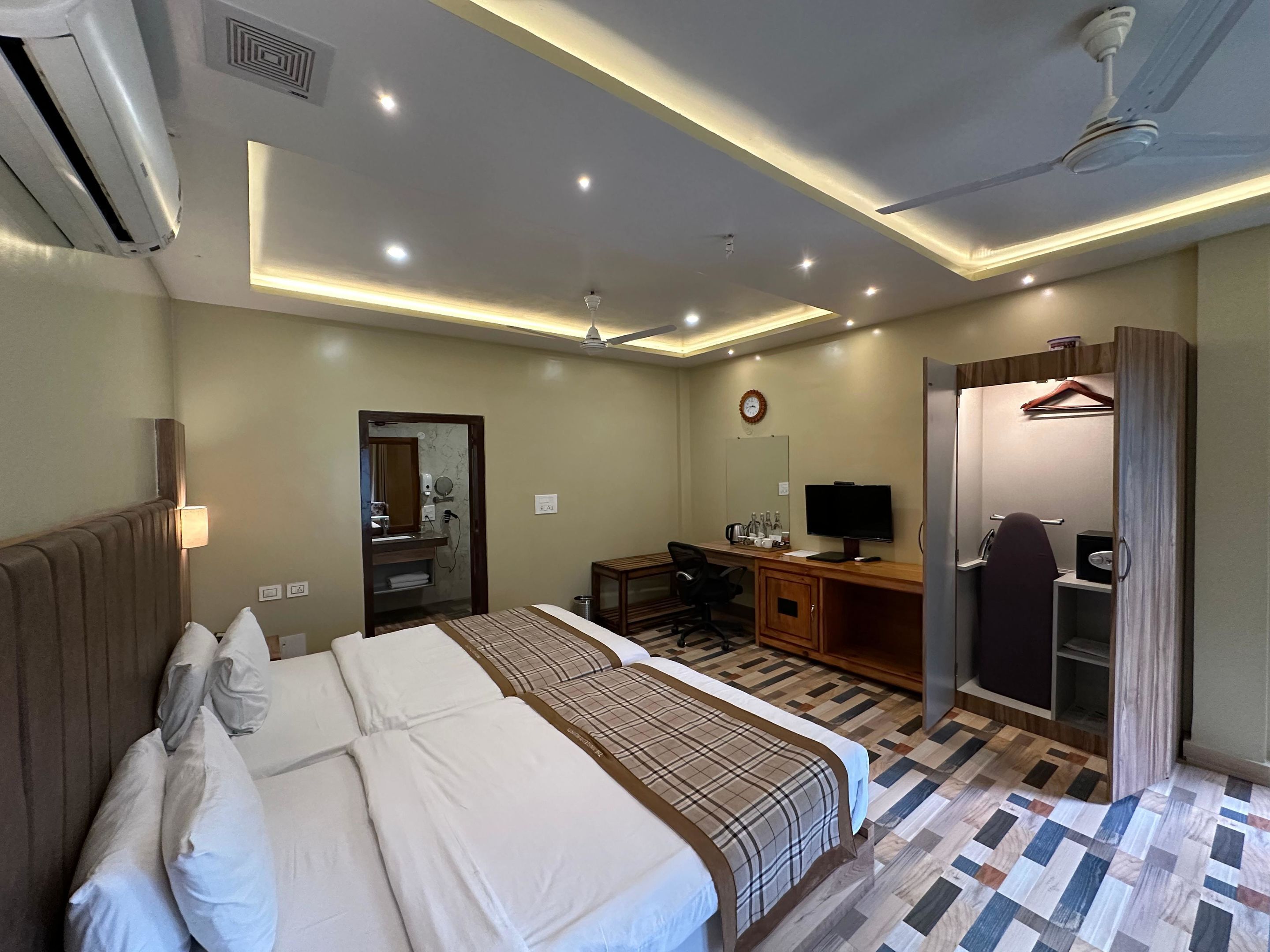 A hotel room with two beds, a desk, a chair, a TV, a wardrobe, and a mirror.