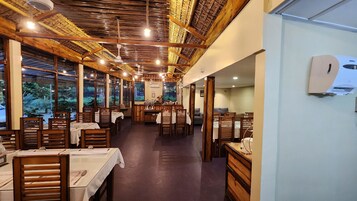 Un restaurante con mesas y sillas de madera, ventanas amplias y un techo alto con vigas a la vista.