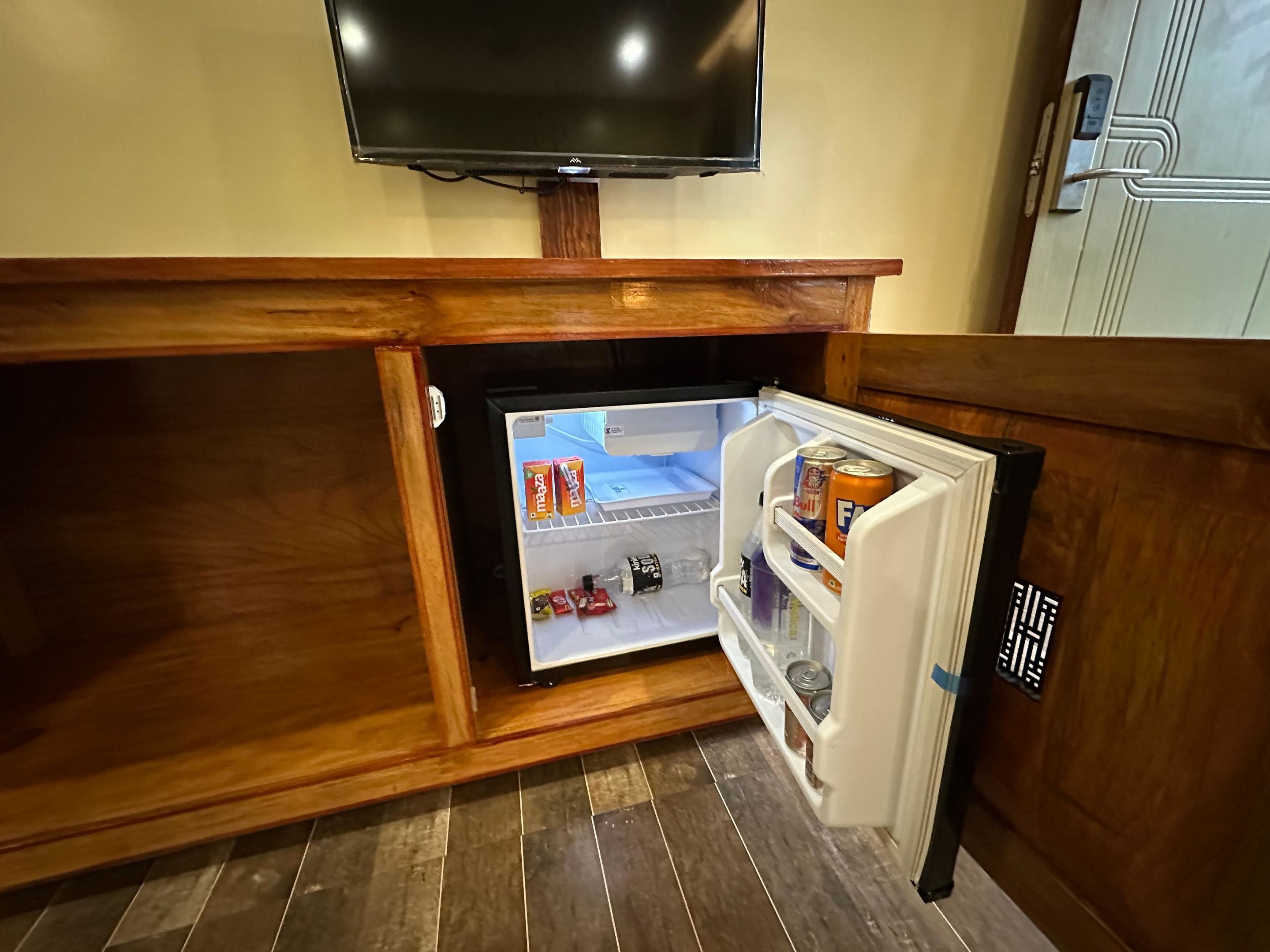 Een compacte koelkast met een ingebouwde televisie, geplaatst onder een houten kastje in een keuken.