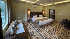 Una camera d'albergo con un letto grande, un divano più piccolo, una scrivania e un angolo doccia.