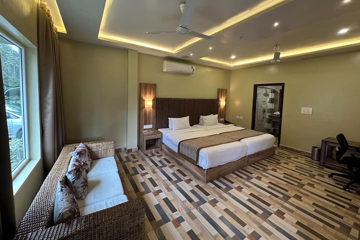 A hotel room with a large bed, a smaller sofa, a desk, and a shower area.
