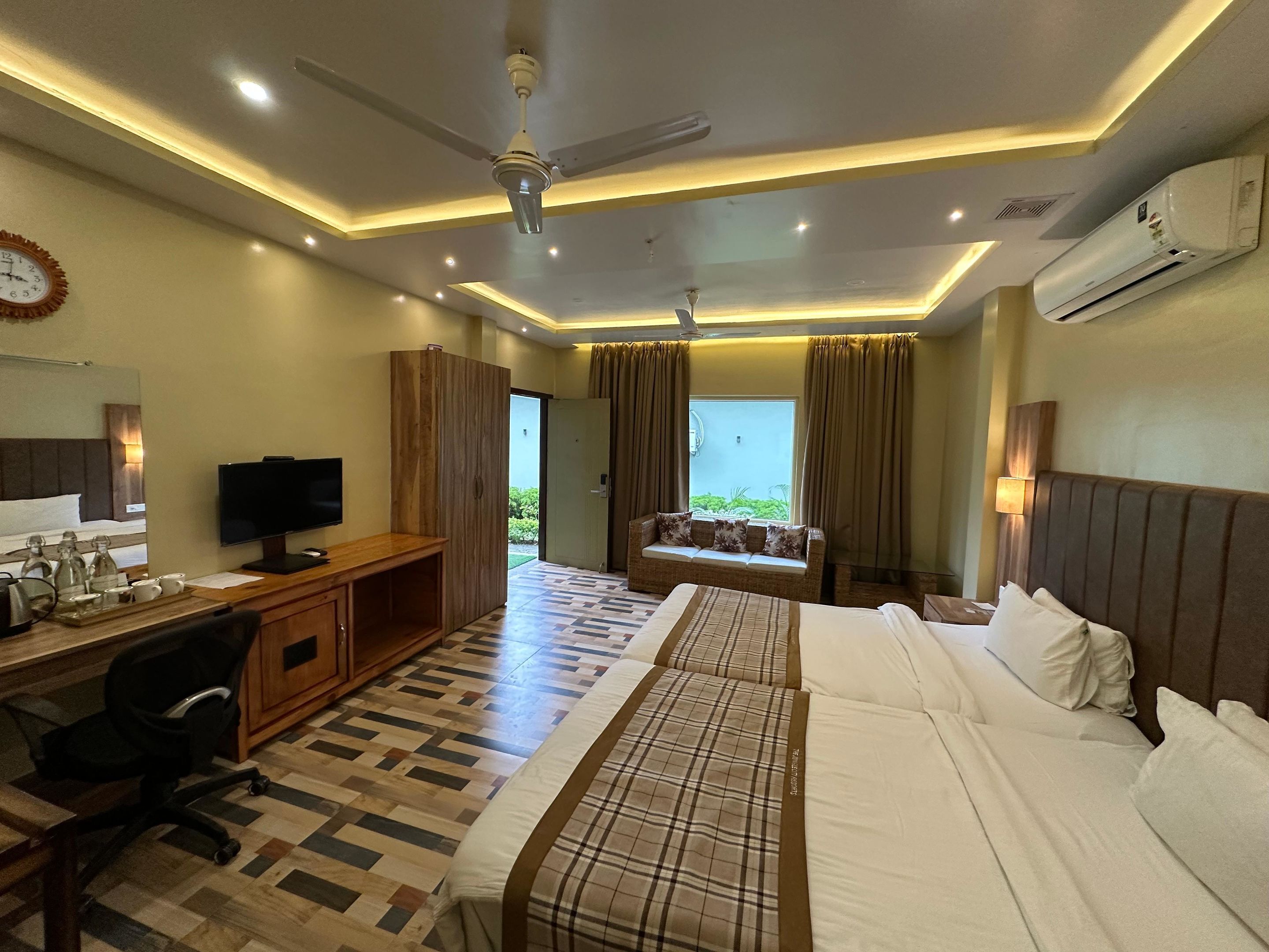 Ein Hotelzimmer mit Bett, Schreibtisch inklusive Computer, Fernseher, Kleiderschrank und einem fenster mit Vorhängen.