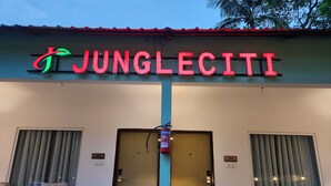 Un edificio con un cartello che riporta la scritta "JUNGLECITI" e due porte. Di fuori, sono disposti dei divanetti in vimini.