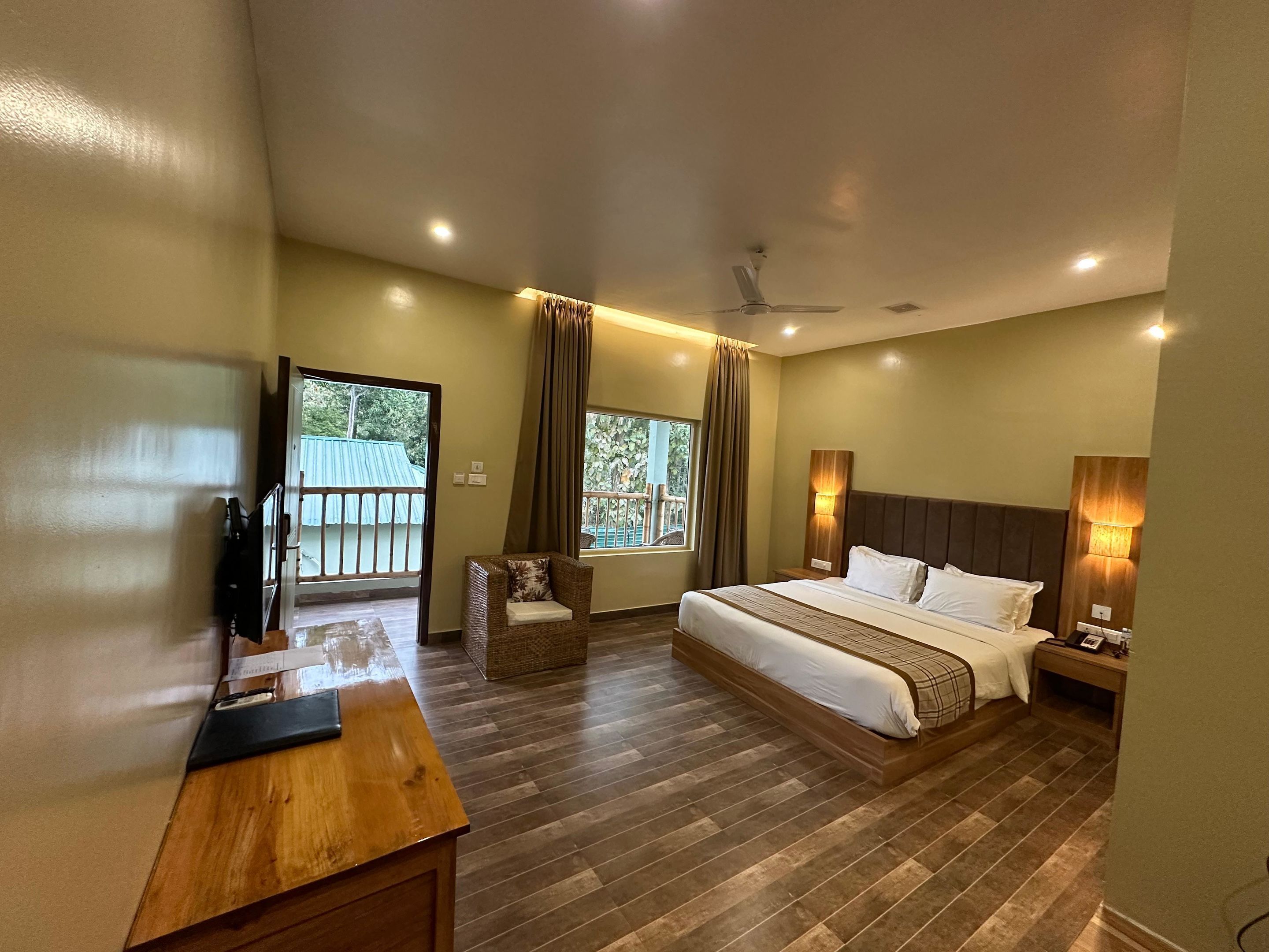 A hotel room with a bed, a desk, a chair, a ceiling fan, and a balcony view.