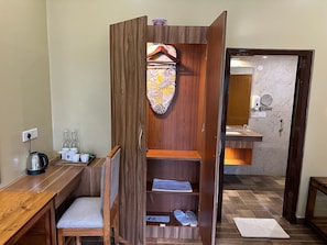 A compact room with a wooden wardrobe, a small desk with a kettle, and a bed with a canopy. - Jungleciti House Kaziranga National Park (Kaliabar)