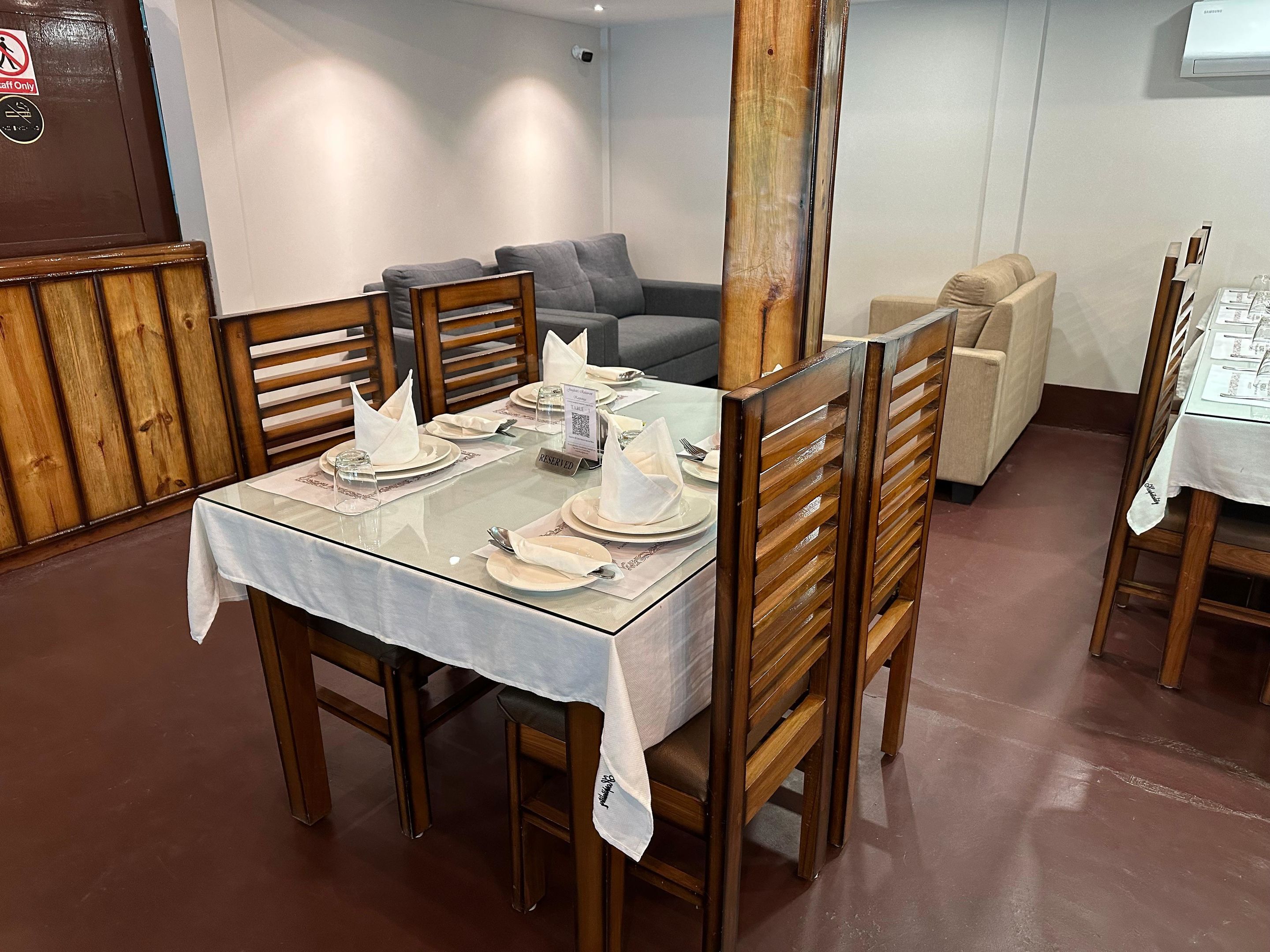 Un comedor con una mesa dispuesta para cuatro, sillas de madera y un sofá al fondo.