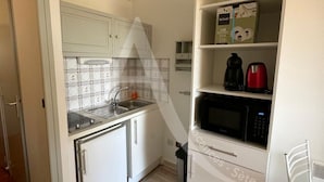Une cuisine compacte avec des meubles blancs, un four à micro-ondes, une bouilloire et un évier.