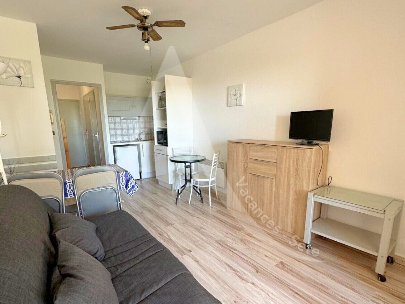 En kompakt opholdsstue med sofa, et lille spisebord med stole, et tekøkken og et fjernsyn på et træskab.
