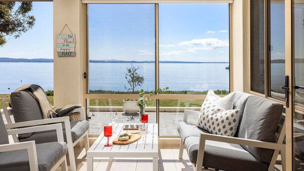En balkong med utsikt över en sjö, ett bord med glas och en tallrik, och en skylt på väggen.
