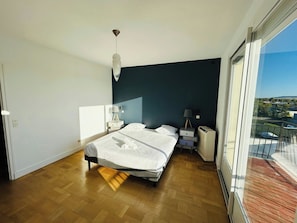 A bedroom with a bed, bedside tables, a lamp, and a view of the outside. - La Maison Léonard | 10 Couchages | Parc des Expos (Reims)