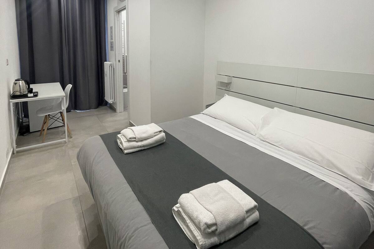 A modern hotel room with a bed, a desk, and a chair.