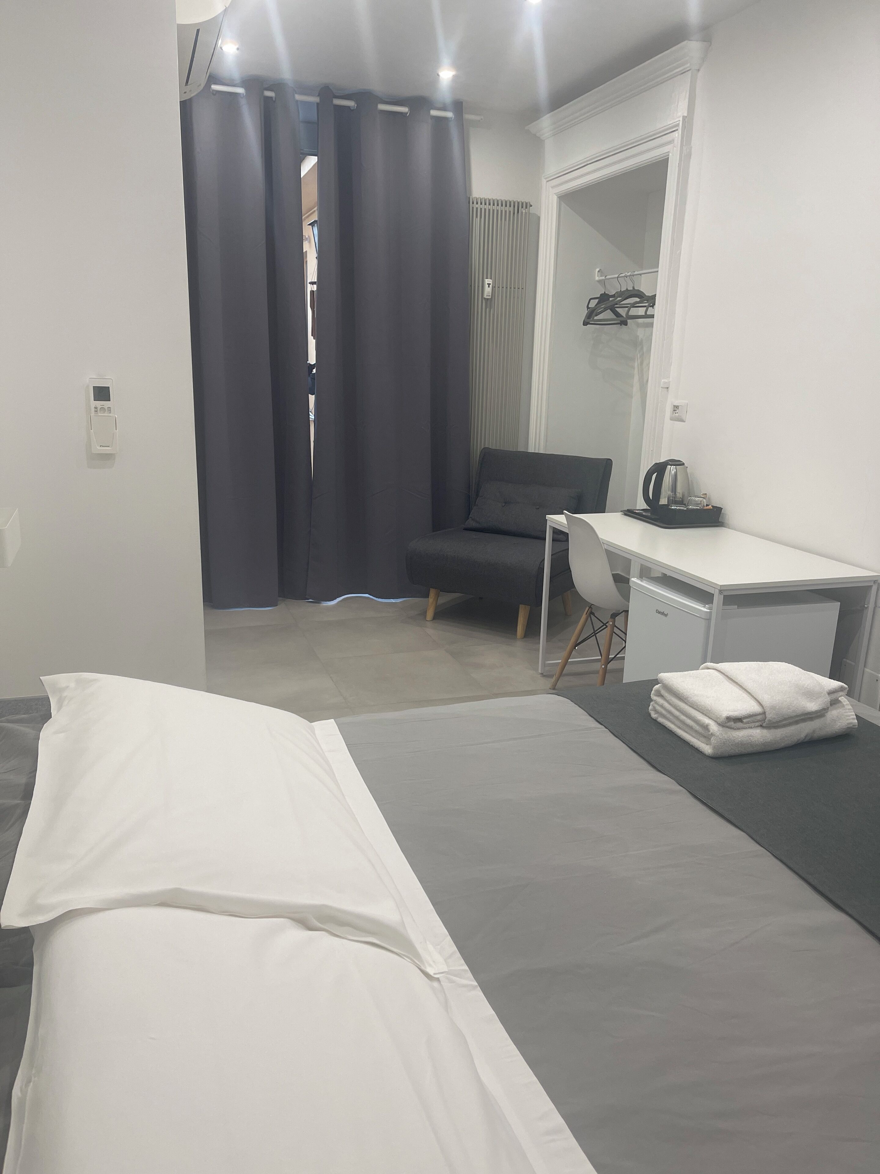 A modern hotel room with a bed, a desk, a chair, and a wardrobe.