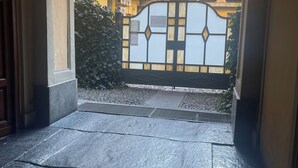A view through a gate into a courtyard with a tiled floor, a metal gate, and a building with balconies in the background. - Porta Nuova Suite 57  (Turin)
