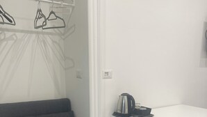 A modern room with a grey sofa, a white desk with a chair, and a kettle on the desk. - Porta Nuova Suite 57  (Turin)