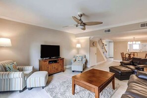 Un salon doté d’un téléviseur à écran plat, de canapés à rayures, d’une table basse en bois, d’un ventilateur de plafond et d’un escalier menant à un autre niveau.
