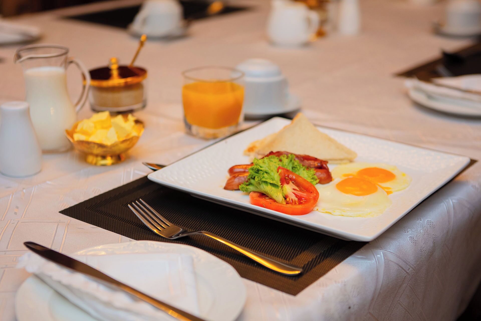 Un desayuno con un plato de huevos, tocino y verduras, un vaso de zumo de naranja y una jarra de leche sobre una mesa.
